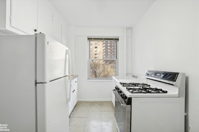 kitchen featuring white fridge, light tile patterned floors, white cabinets, and range with gas cooktop