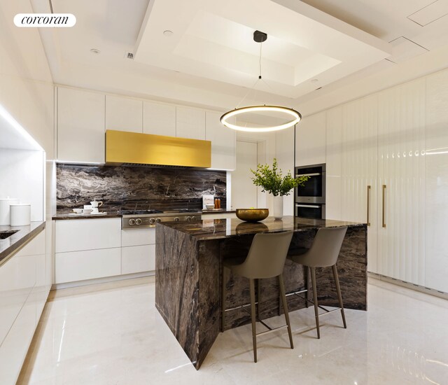 kitchen featuring white cabinets, a kitchen island, modern cabinets, decorative light fixtures, and a tray ceiling