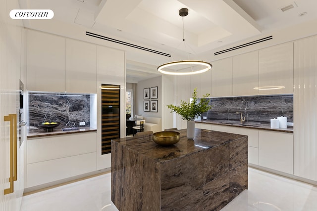 kitchen with tasteful backsplash, modern cabinets, decorative light fixtures, a tray ceiling, and a sink