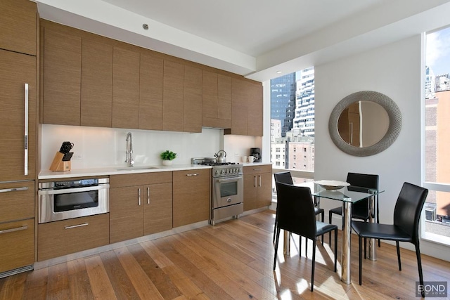 kitchen featuring light wood finished floors, light countertops, appliances with stainless steel finishes, brown cabinetry, and a sink