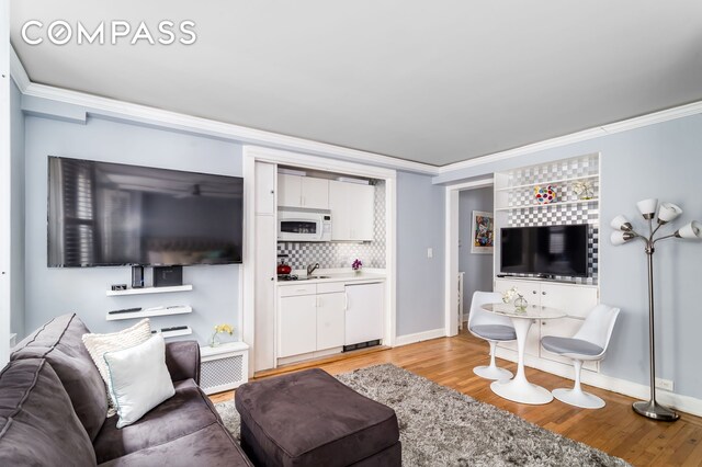 living area with baseboards, light wood-type flooring, and ornamental molding