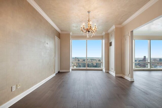 empty room with crown molding, a healthy amount of sunlight, dark hardwood / wood-style flooring, and a notable chandelier