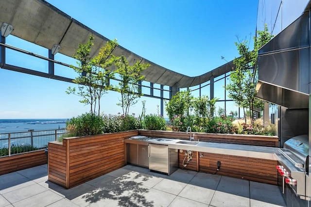 view of patio / terrace with a sink, a water view, fence, an outdoor kitchen, and grilling area