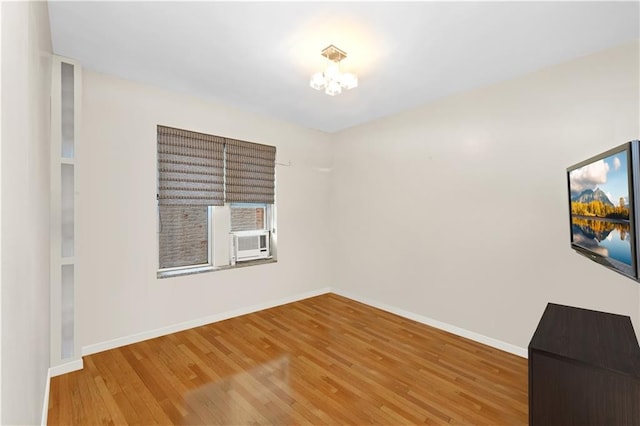 empty room featuring wood-type flooring, a notable chandelier, and cooling unit