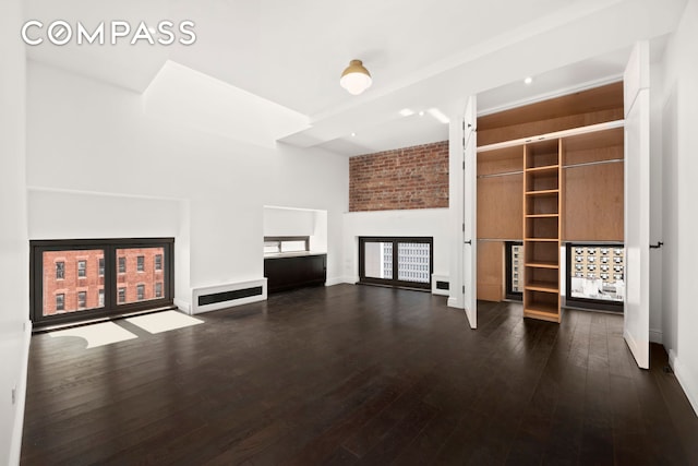 unfurnished living room featuring wood-type flooring, a high ceiling, and baseboards