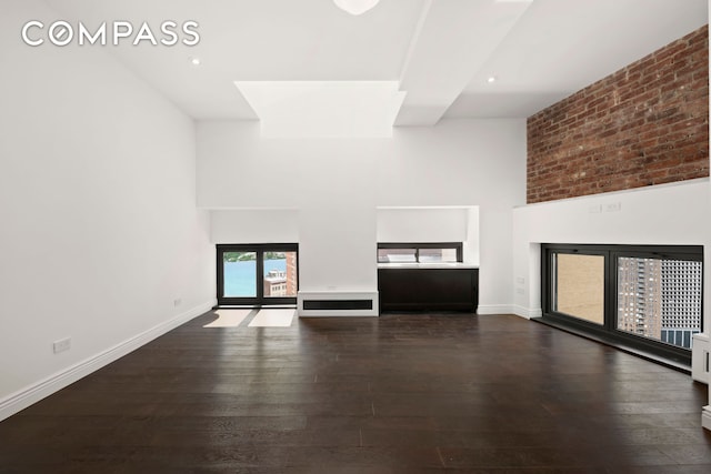 unfurnished living room featuring a towering ceiling, baseboards, and dark wood finished floors