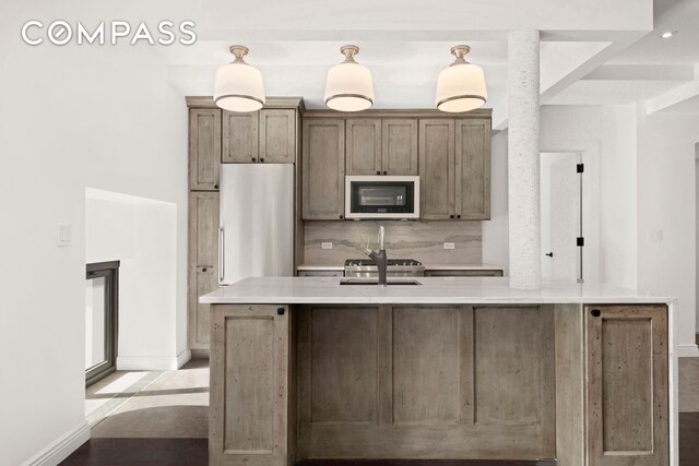 kitchen featuring light countertops, decorative backsplash, white microwave, an island with sink, and stainless steel fridge