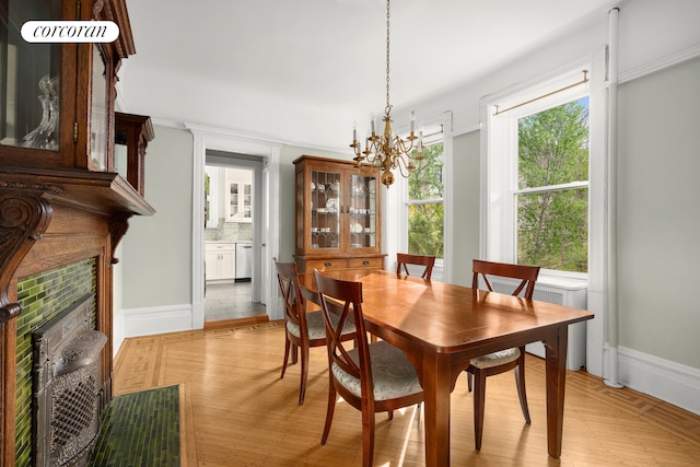 dining room with light wood finished floors, a fireplace, baseboards, and a notable chandelier