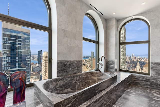 bathroom with a city view, marble finish floor, a tub to relax in, and recessed lighting