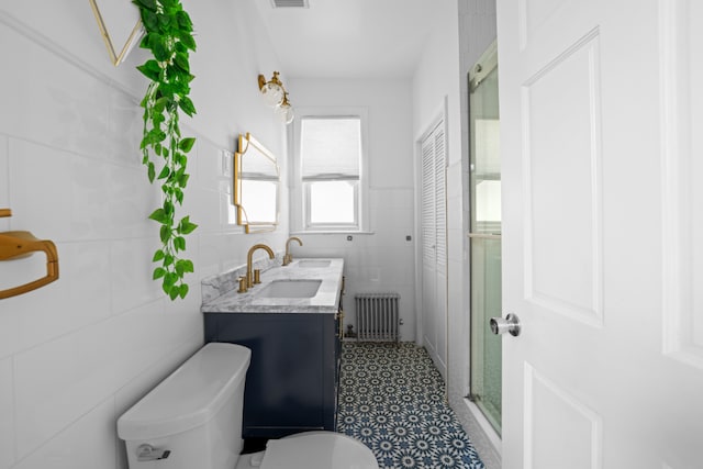 bathroom with radiator heating unit, tile walls, vanity, toilet, and a shower with door