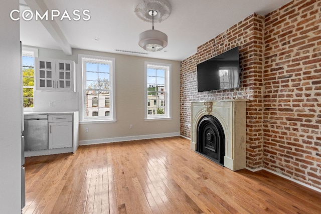 unfurnished living room with a fireplace, beamed ceiling, light hardwood / wood-style floors, and brick wall