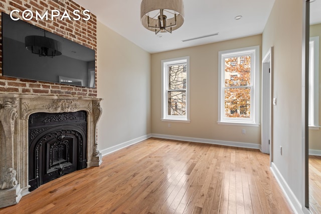 unfurnished living room with visible vents, a fireplace, baseboards, and wood-type flooring