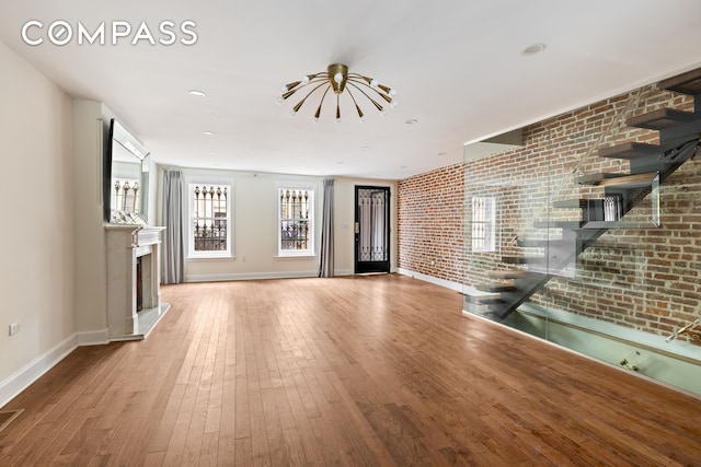 unfurnished living room with hardwood / wood-style floors, a fireplace with raised hearth, baseboards, and brick wall