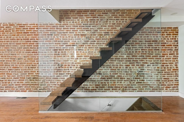 stairway featuring brick wall and wood-type flooring