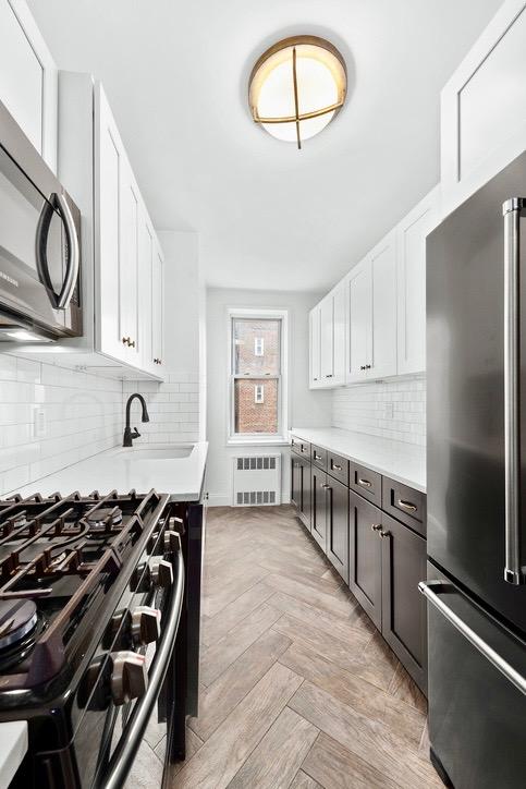 kitchen featuring high quality fridge, white cabinetry, sink, gas stove, and light parquet flooring