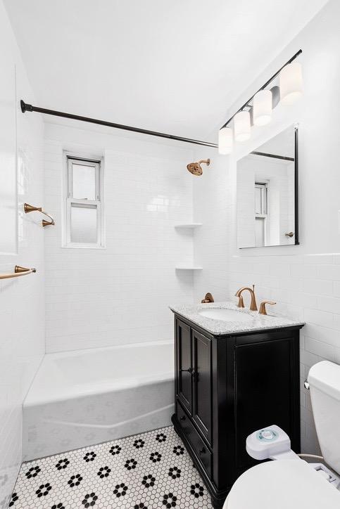 full bathroom with tile walls, tile patterned flooring, vanity, tiled shower / bath combo, and toilet