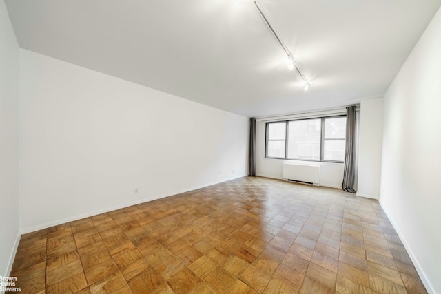 spare room with rail lighting, radiator, and light parquet floors