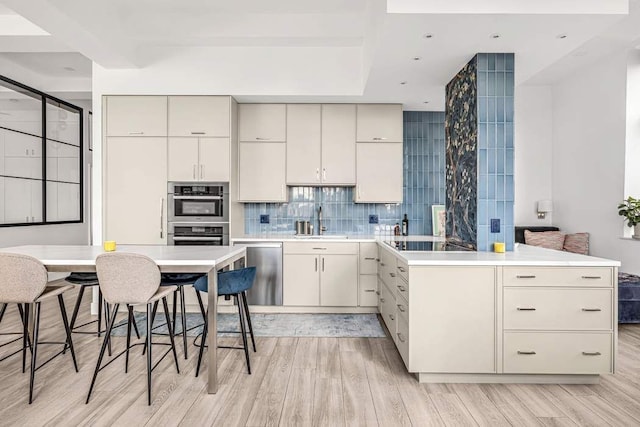 kitchen with decorative backsplash, sink, light wood-type flooring, a kitchen breakfast bar, and stainless steel appliances