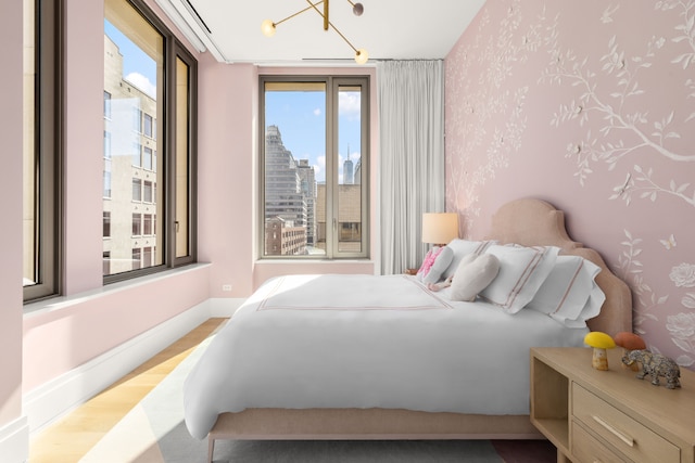 bedroom featuring a city view, light wood finished floors, multiple windows, and wallpapered walls