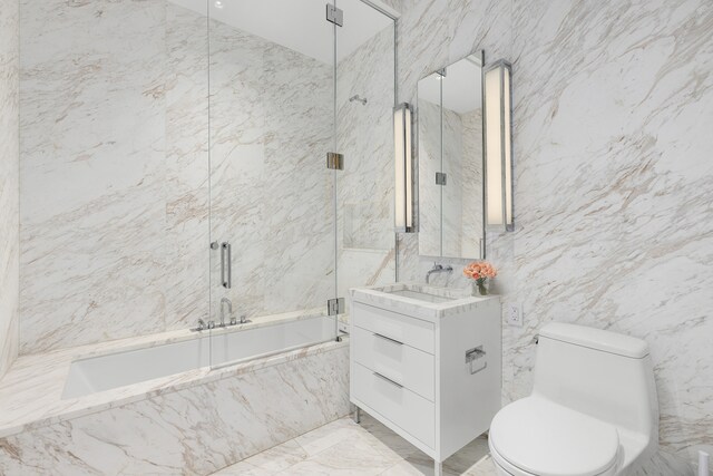 bathroom featuring marble finish floor, tile walls, toilet, vanity, and a combined bath / shower with marble appearance