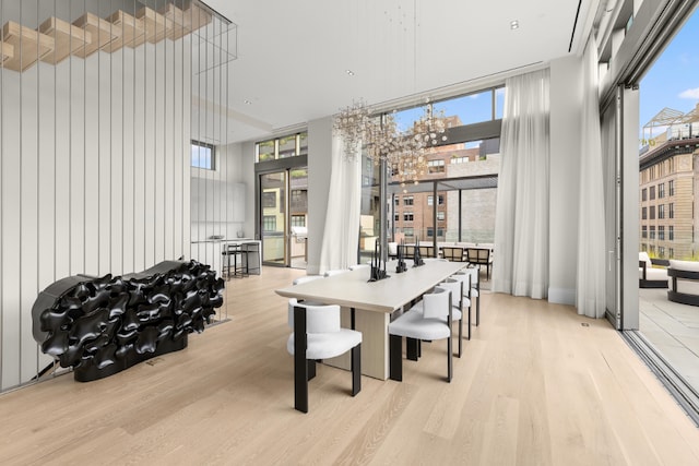 dining area featuring a towering ceiling, light wood-style floors, and floor to ceiling windows