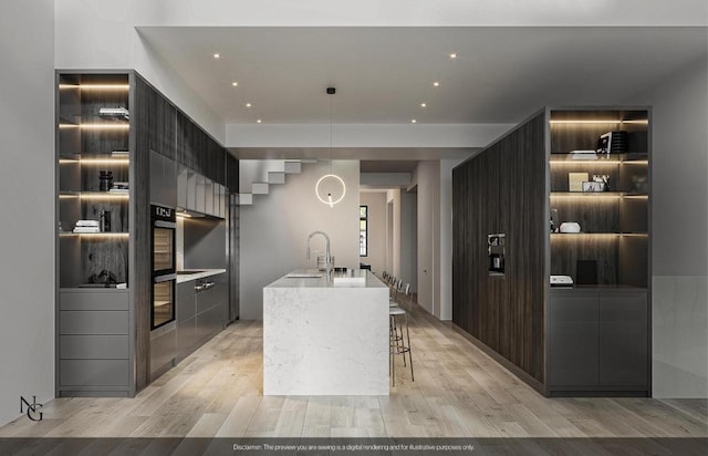 kitchen featuring sink, oven, a kitchen breakfast bar, light hardwood / wood-style floors, and a center island with sink