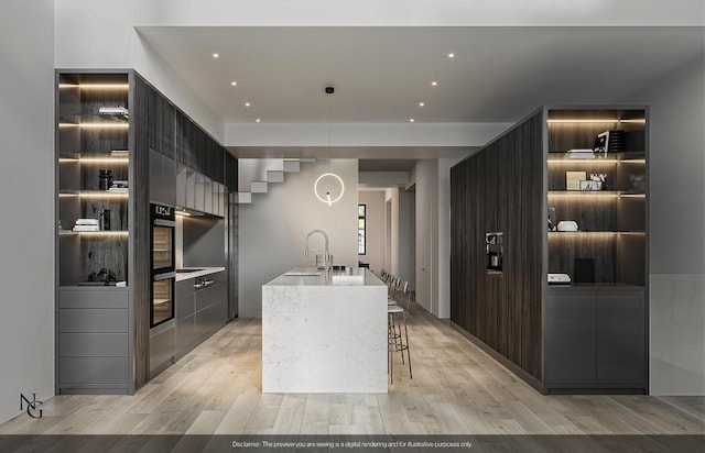 kitchen featuring modern cabinets, a kitchen island with sink, light countertops, light wood-type flooring, and a sink