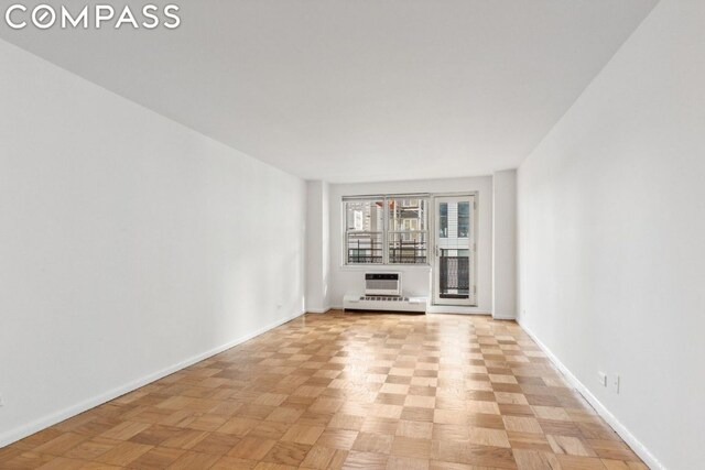 unfurnished living room featuring light parquet floors, an AC wall unit, and baseboard heating