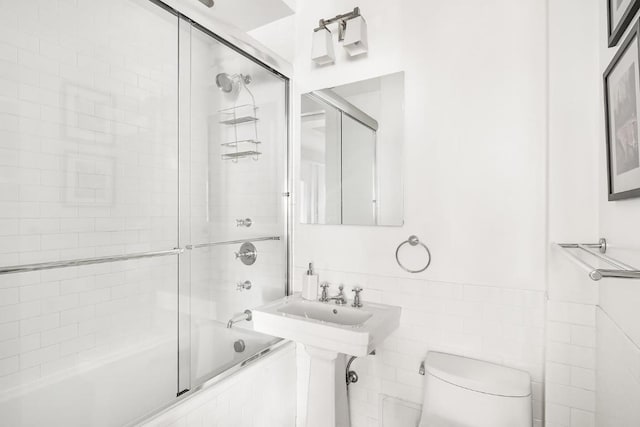 bathroom with tile walls, enclosed tub / shower combo, and toilet