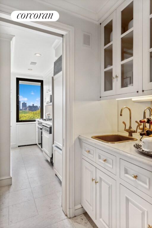 kitchen featuring crown molding, visible vents, glass insert cabinets, white cabinets, and a sink