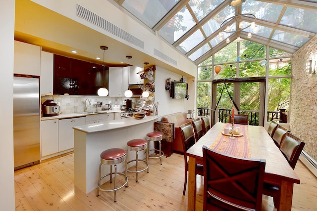 dining room with light wood finished floors, a skylight, and high vaulted ceiling