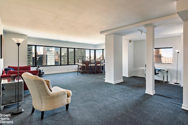 living room featuring dark carpet, plenty of natural light, and decorative columns