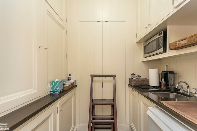 61 E 86th St Unit 6, New York City, NY 10028 - kitchen with stainless steel microwave, dark countertops, a sink, and white cabinetry