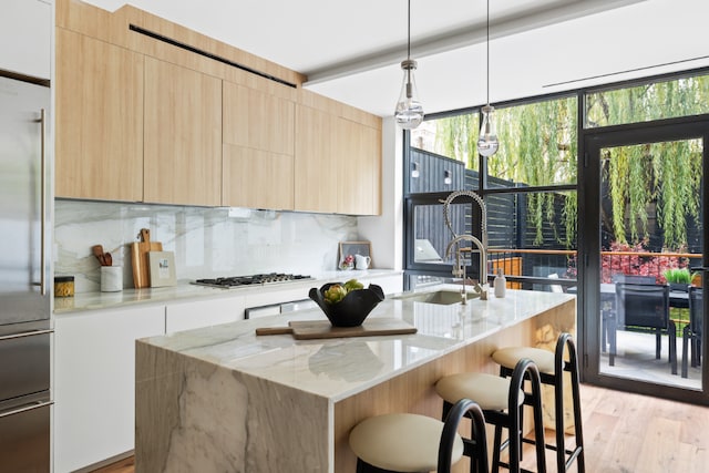 kitchen featuring stainless steel appliances, light stone countertops, a center island with sink, and decorative light fixtures