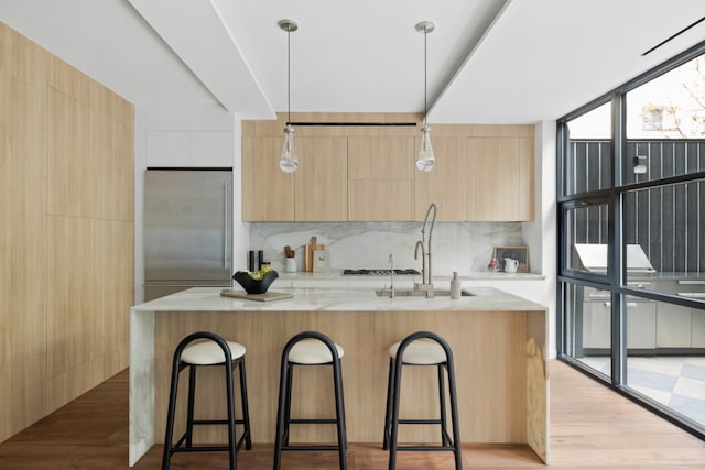 kitchen featuring built in fridge, decorative light fixtures, a center island with sink, and modern cabinets