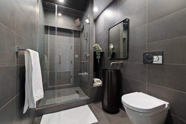 bathroom featuring toilet, a stall shower, tile patterned flooring, and tile walls