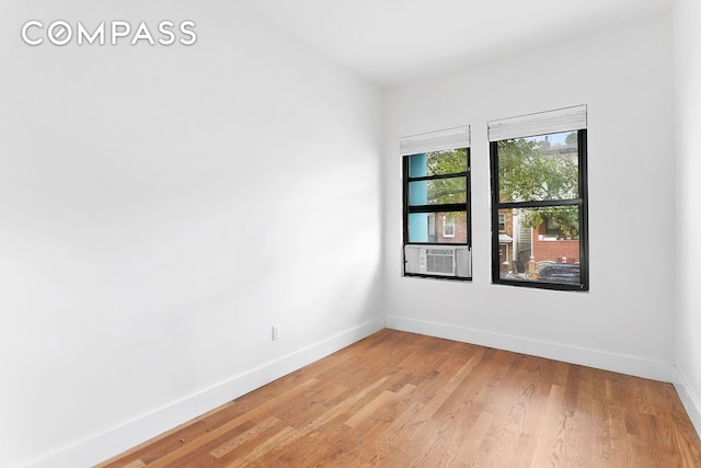 empty room featuring cooling unit, light wood-style flooring, and baseboards