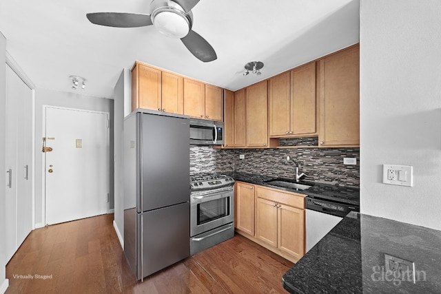 kitchen featuring sink, dark stone countertops, appliances with stainless steel finishes, dark hardwood / wood-style flooring, and decorative backsplash