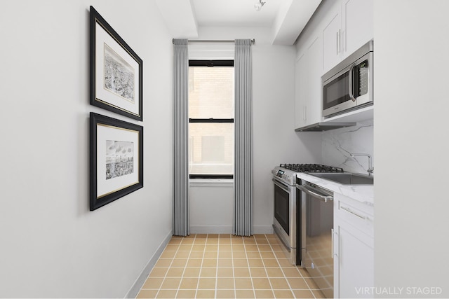 kitchen featuring light tile patterned floors, stainless steel appliances, white cabinets, light countertops, and backsplash