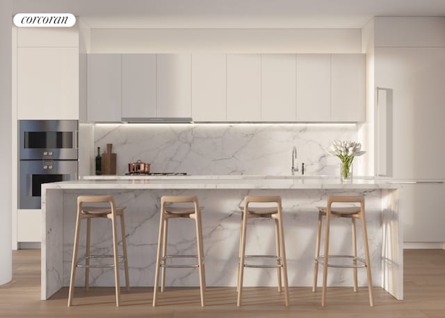 kitchen featuring backsplash, white cabinets, a kitchen bar, and double oven