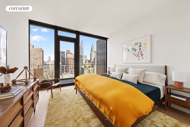 bedroom with a wall of windows, a view of city, visible vents, and light wood-type flooring