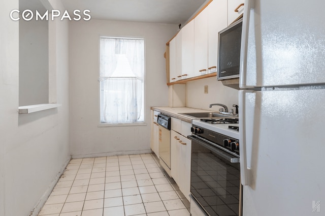 kitchen featuring black microwave, a sink, white cabinetry, freestanding refrigerator, and gas stove