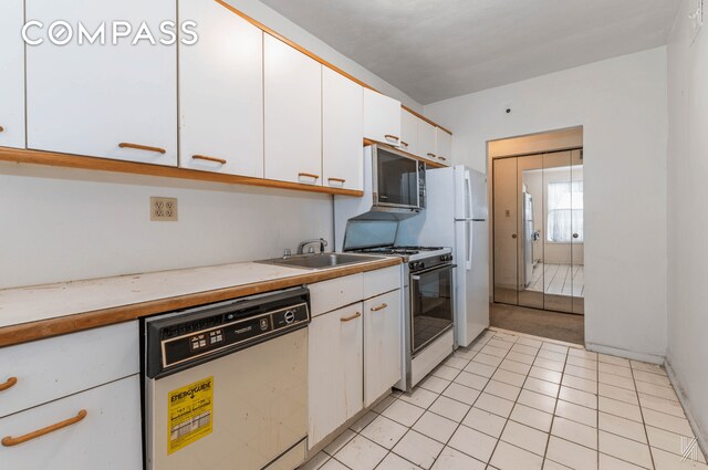 kitchen with light tile patterned floors, white appliances, a sink, white cabinets, and light countertops