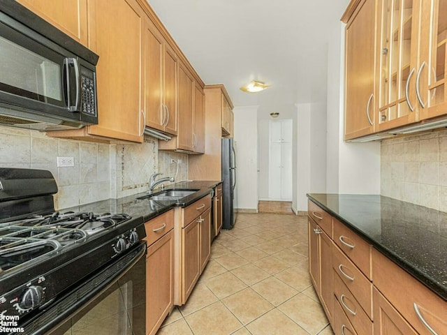 kitchen with dark stone countertops, brown cabinetry, a sink, and black appliances