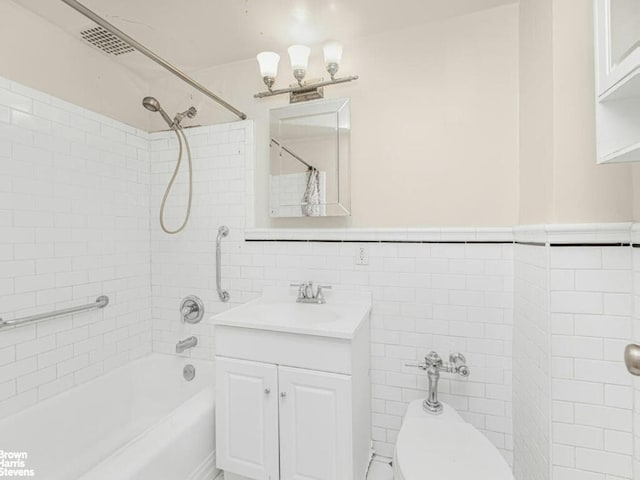 bathroom featuring toilet, a wainscoted wall, vanity, tile walls, and washtub / shower combination