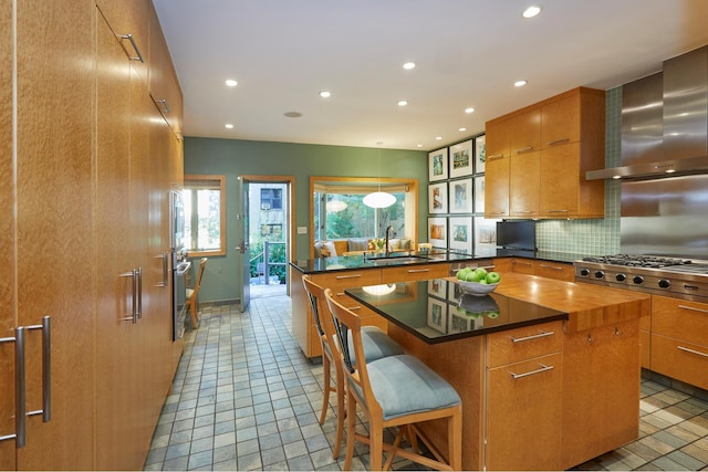 kitchen featuring a breakfast bar, a center island, decorative backsplash, a sink, and wall chimney exhaust hood