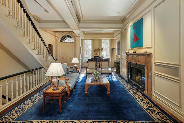 living area featuring beam ceiling, a premium fireplace, ornamental molding, coffered ceiling, and stairs