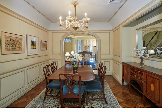 dining area featuring arched walkways, a notable chandelier, a decorative wall, visible vents, and ornamental molding