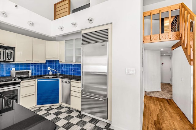 kitchen featuring a sink, light wood-type flooring, appliances with stainless steel finishes, dark countertops, and backsplash