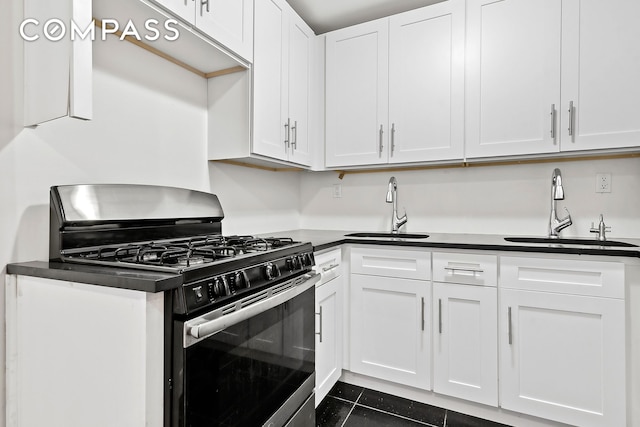 kitchen featuring a sink, stainless steel gas stove, dark countertops, and dark tile patterned floors